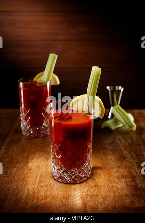 Riflettori puntati su due bicchieri di cristallo pieno di Bloody Mary cocktail, con un sedano guarnire, girato su un antico tavolo di legno alto. Foto Stock