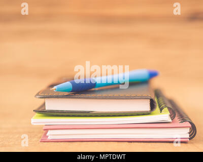 Accessori per ufficio tra cui nota libri e penna blu su sfondo di legno. L'istruzione e la concezione di business. Foto Stock