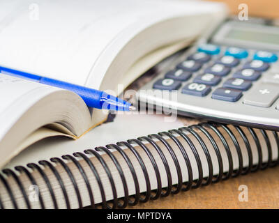 Accessori per ufficio tra cui libri, penna blu e calcolatrice su sfondo di legno. L'istruzione e la concezione di business. Foto Stock