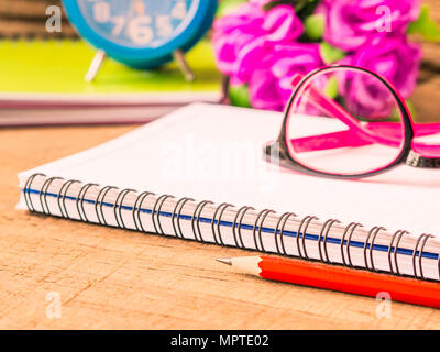 Accessori per ufficio tra cui note book, matita rossa, rosa bicchieri e sveglia su sfondo di legno. L'istruzione e la concezione di business. Foto Stock