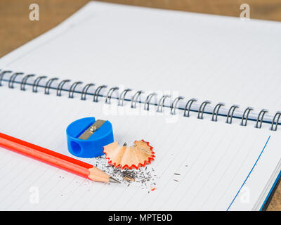 Accessori per ufficio tra cui note book, matita rossa e blu sharpener su sfondo di legno. L'istruzione e la concezione di business. Foto Stock