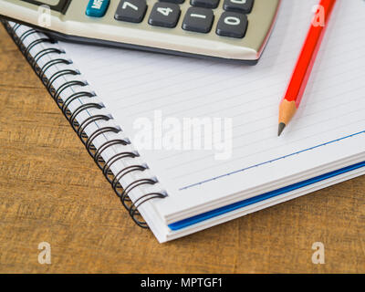 Accessori per ufficio tra cui note book, matita rossa e calcolatrice su sfondo di legno. L'istruzione e la concezione di business. Foto Stock