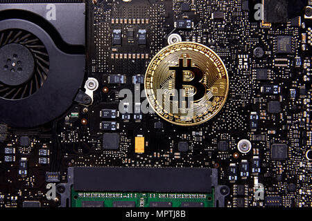 Un Bitcoin moneta fisica seduto su una scheda madre del computer con un ventilatore e RAM. È la prima moneta decentralizzata Foto Stock