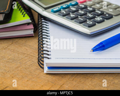 Accessori per ufficio tra cui note book, penna blu e calcolatrice su sfondo di legno. L'istruzione e la concezione di business. Foto Stock