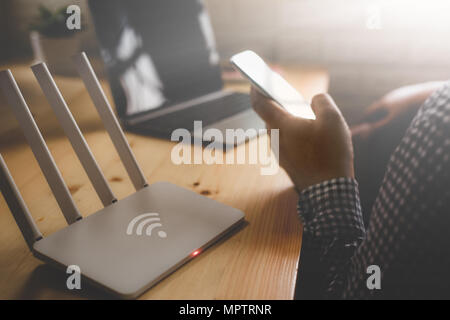 Primo piano di un router wireless e un uomo utilizza lo smartphone sul salotto di casa ofiice Foto Stock