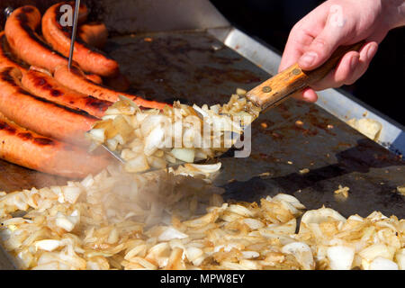 Giovane Maschio lato con la spatola girando le cipolle tritate su un grill, grigliare le cipolle. Venditore ambulante. Foto Stock