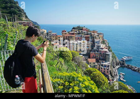 Un giovane ragazzo per scattare una foto della splendida vista della città di Manarola. È uno dei cinque famosi villaggi colorati del Parco Nazionale delle Cinque Terre in Italia Foto Stock