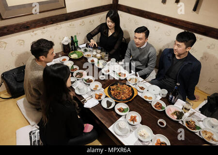 I giovani coreani seduti intorno ad un basso tavolo di legno sui tappetini del pavimento e cenando al tipico Hanjeongsik, un tradizionale pasto coreano a portata completa nella città di Seul, capitale della Repubblica di Corea comunemente conosciuta come Corea del Sud Foto Stock