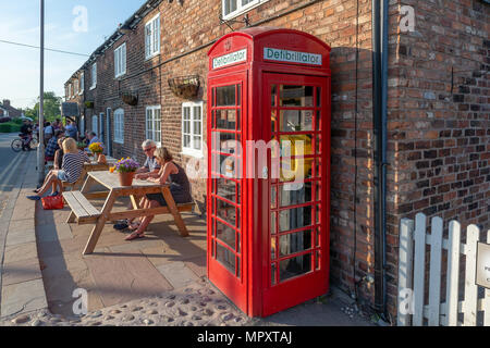 Red K2 nella casella telefono utilizzato come una libreria e stazione del defibrillatore al di fuori del Hatton Arms public house di Hatton, Cheshire, Inghilterra, Regno Unito Foto Stock