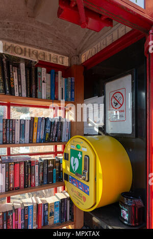 Red K2 nella casella telefono utilizzato come una libreria e stazione del defibrillatore al di fuori del Hatton Arms public house di Hatton, Cheshire, Inghilterra, Regno Unito Foto Stock