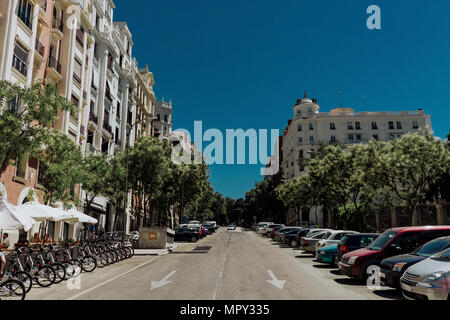 Automobili e biciclette parcheggiate su strada in mezzo a edifici contro il cielo blu e chiaro durante la giornata di sole Foto Stock