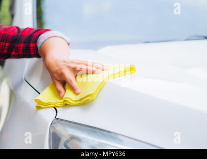 Mano con giallo panno in microfibra per la pulizia auto bianco. Foto Stock