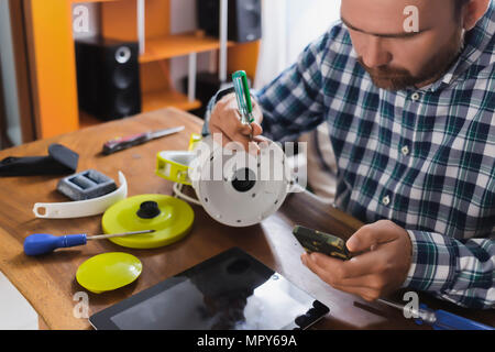 Uomo che ripara apparecchio mentre utilizzando smart phone a casa Foto Stock
