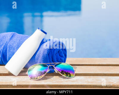 Occhiali da sole, asciugamano blu e crema solare a lato della piscina. Vacanze, spiaggia, estate concetto di viaggio Foto Stock