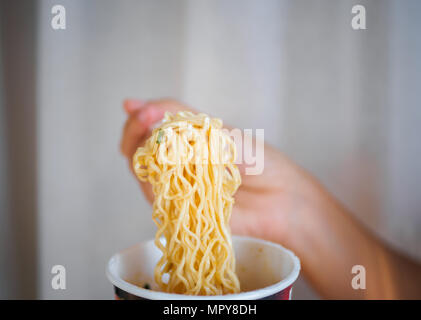 Mano che tiene la forcella per mangiare piccante tagliatelle istante in coppa, sodio dieta ad alto rischio di insufficienza renale. Mangiare sano concetto. Foto Stock