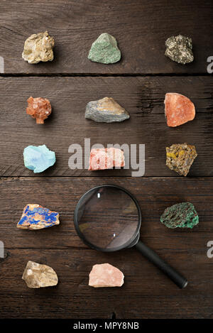 Vista aerea di gemme colorate con lente di ingrandimento sul tavolo di legno Foto Stock