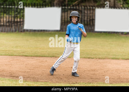 Little League Baseball all star in uniforme blu che conducono fuori sull'infield sporco come baserunner. Foto Stock