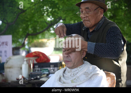Nanjin, Nanjin, Cina. Xxiv Maggio, 2018. Nanjing, Cina-24Maggio 2018: Il 79-year-old street barbiere Wang Xiaofu taglia i capelli per un uomo sulla strada di Nanjing East cinese della provincia di Jiangsu. Wang ha iniziato a imparare barbery all'età di 13 ed è stata una strada barbiere per 66 anni. Credito: SIPA Asia/ZUMA filo/Alamy Live News Foto Stock