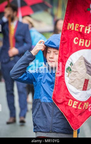 "Delph, UK. 25 maggio 2018. Un giovane titolare di banner lotte con la pioggia come egli cammina lungo la processione durante l'annuale "Pentecoste" passeggiate attraverso il villaggio di "Delph nel distretto di Saddleworth, Greater Manchester. Credito: Matthew Wilkinson/Alamy Live News Foto Stock