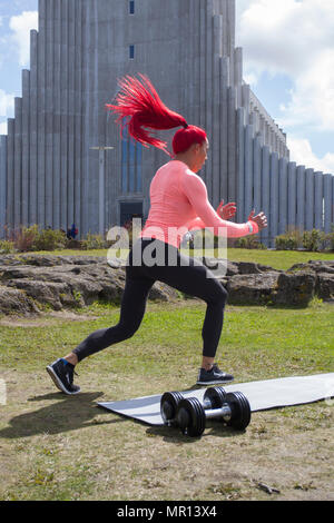 Reykjavík, Islanda. 25/05/2018 Meteo. Pomeriggio di sole nella capitale come Hannah Eden (Eden fitness training online) esegue una routine per un esercizio video, di fronte alla chiesa Hallgrímskirkja che è Reykjavik il punto di riferimento principale. Foto Stock