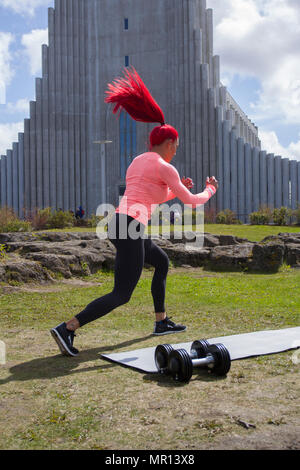 Reykjavík, Islanda. 25/05/2018 Meteo. Pomeriggio di sole nella capitale come Hannah Eden (Eden fitness training online) esegue una routine per un esercizio video, di fronte alla chiesa Hallgrímskirkja che è Reykjavik il punto di riferimento principale. Foto Stock