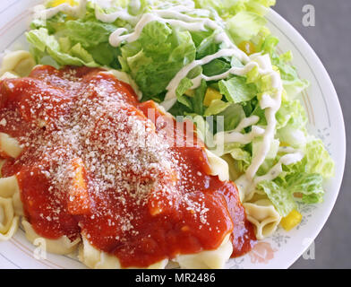 Formaggio Ravioli fatti in casa con salsa di pomodoro condito con parmigiano grattugiato. Insalata con condimento cremoso sul lato Foto Stock