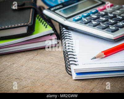 Accessori per ufficio tra cui note book, matita rossa e calcolatrice su sfondo di legno. L'istruzione e la concezione di business. Foto Stock