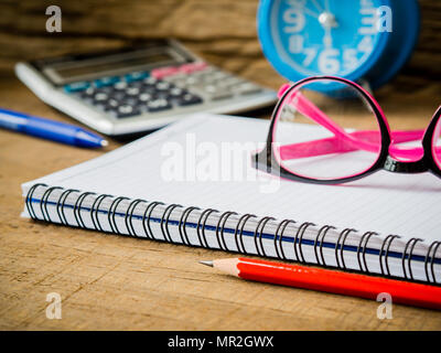 Accessori per ufficio tra cui note book, matita rossa, rosa bicchieri e calcolatrice su sfondo di legno. L'istruzione e la concezione di business. Foto Stock