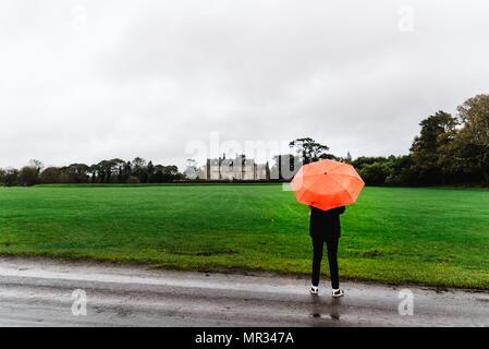 Killarney, Irlanda - 11 Novembre 2017: donna non identificato con ombrello rosso in Muckross House e giardini contro il cielo nuvoloso. Si tratta di un palazzo situato Foto Stock