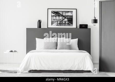 Cuscini modellato sul letto in grigio e bianco interiore camera da letto con poster e lampada Foto Stock