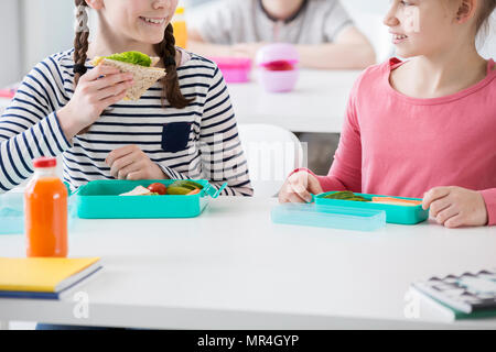 Close-up della ragazza sorridente mangiare toast eco durante la pausa colazione a scuola Foto Stock