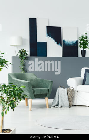 Poltrona verde in piedi in bianco salotto interno con piante fresche e dipinti di arte moderna Foto Stock