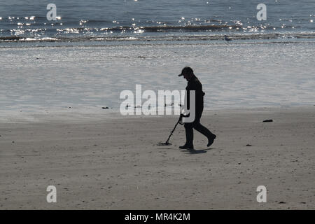 Uomo in silhouette camminando lungo una spiaggia con la bassa marea con un rivelatore di metalli. Foto Stock