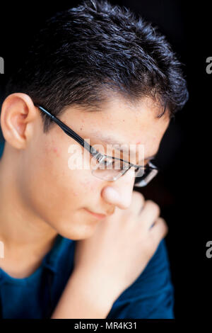 Ritratto di un adolescente in posa con un piccolo sorriso sul suo volto in uno sfondo scuro da indossare con cappuccio verde T-shirt.chiave di basso verticale. Foto Stock