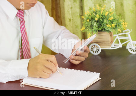 Business man iscritto su notebook e cercando lavoro sul telefono nel luogo di lavoro Foto Stock