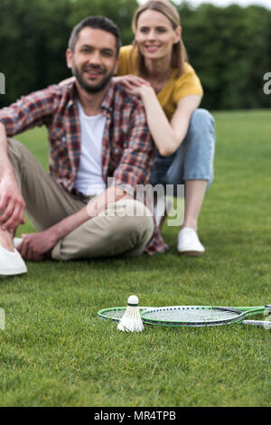 Volano e badminton racchette giacente su erba, felice coppia seduta dietro Foto Stock