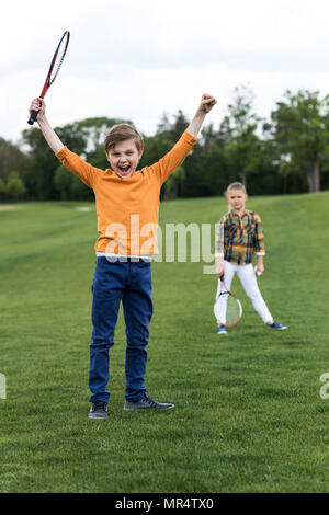 Happy Child holding badminton racchetta e trionfante mentre i gemelli in piedi dietro Foto Stock