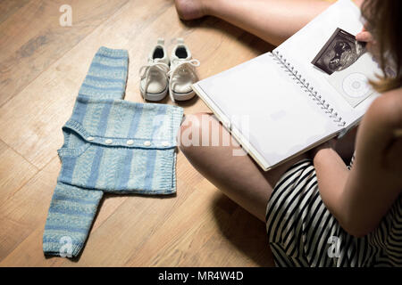 Donna immissione del bambino in sonogram baby del primo anno del libro di memoria. Baby vestiti e scarpe da ginnastica la posa sul pavimento Foto Stock