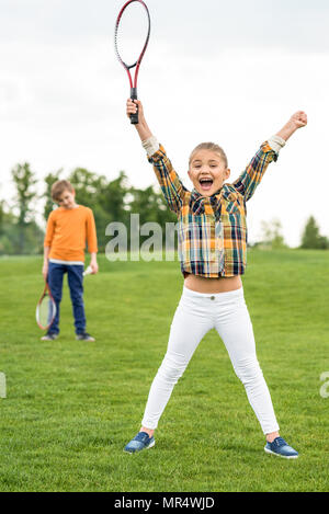 Happy Child holding badminton racchetta e trionfante mentre i gemelli in piedi dietro Foto Stock