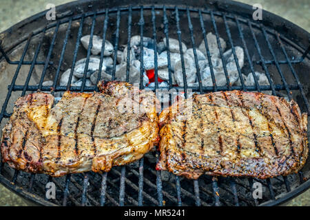 Due bistecche di carne stagionata seduto sopra la brace su un piccolo grill all'aperto. Foto Stock