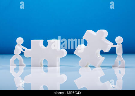 Due figure umane risolvendo puzzle contro sfondo blu Foto Stock