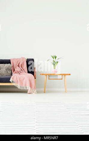 Impianto sul tavolo di legno accanto al lettino scuro con coperta rosa contro la parete con copia spazio in piano luminoso interno con moquette a motivi geometrici Foto Stock