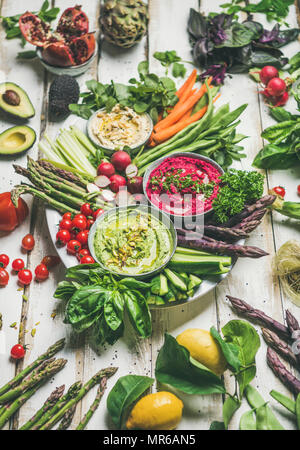 Sana estate raw vegan snack piastra. Ceci, barbabietole, spinaci hummus salse con colorati di verdure fresche e verdi su tavolo bianco sullo sfondo. Cle Foto Stock