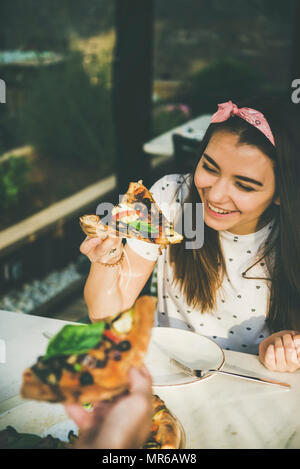 Giovani caucasici felice coppia seduta a tavola godendo appena sfornato pizza in outdoor cucina italiana cafè sulla chiara soleggiata giornata estiva Foto Stock