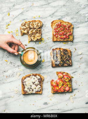 Una sana prima colazione, snack. Piatto di laici vegano toast integrali con frutta, semi, dadi, burro di arachidi e donna prendendo mano tazza di espresso su marb Foto Stock