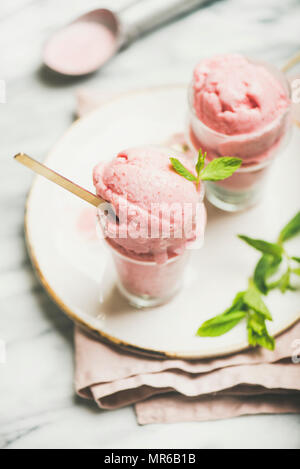 Una sana a basso contenuto calorico dessert estivo. In casa di yogurt alla fragola gelato con menta fresca in bicchieri sulla lastra di marmo grigio sfondo tabella. Pulire Foto Stock