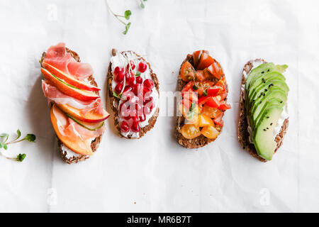 Varietà di bruschette con avecado, prosciutto, pomodori e i semi di melograno su sfondo bianco Foto Stock