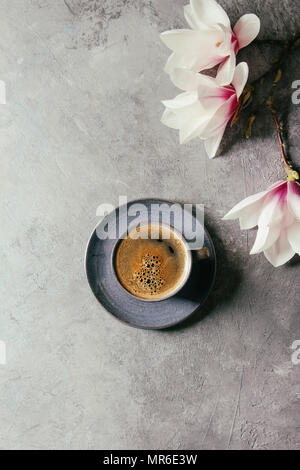 Coppa del blu di nero caffè espresso e fiori di primavera magnolia rami su grigio Sfondo texture. Vista superiore, spazio. Molla della scheda Messaggi di saluto, Foto Stock