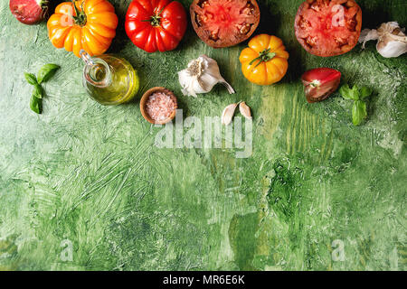 Varietà di rosso e giallo pomodori organici con olio d'oliva, aglio, sale per insalata su una texture verde dello sfondo. Vista superiore, copia dello spazio. Foto Stock