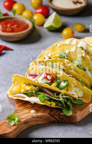 Varietà di mais vegetariano tacos con verdure, insalata verde, peperoncino servita sul tagliere di legno con panna e pomodoro salse con ingredien Foto Stock